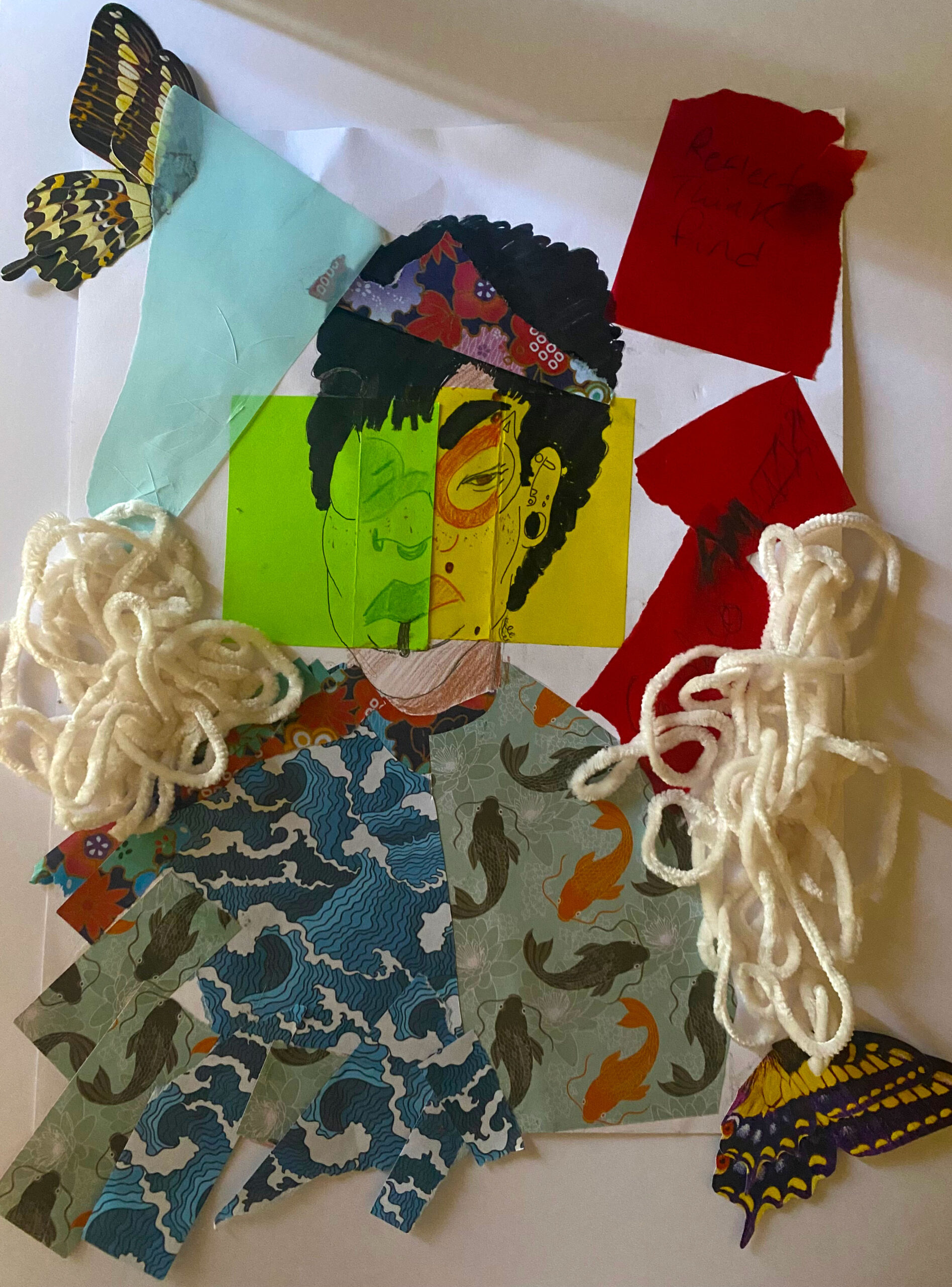 A collage on a wall. In the center is a self-portrait of a woman with dark black hair. She wears glasses. Her left eye is closed, while her right one looks out at the audience. Her face is drawn on two pieces of paper – one yellow, one green. Her clothing is made of wrapping paper featuring Japanese motifs. There are a couple of butterflies around her, pieces of red paper, and string.